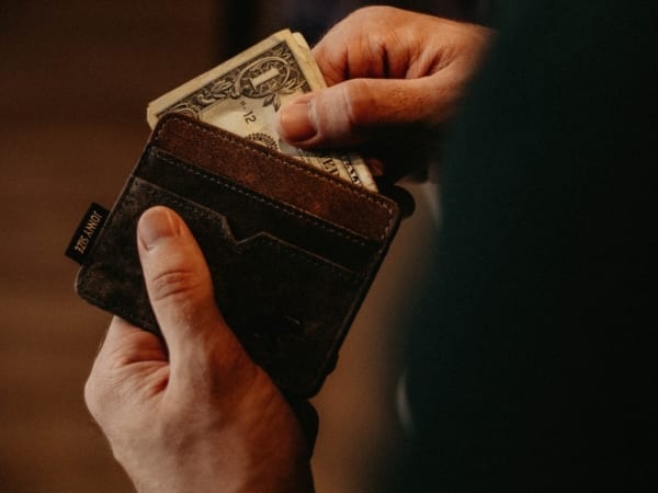Hands holding a wallet, removing folded one dollar bill.