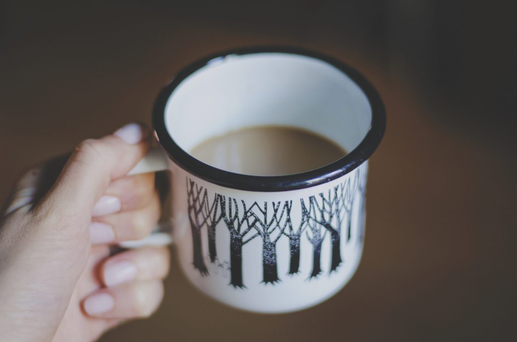 A hand holding a coffee cup decorated with wintery trees