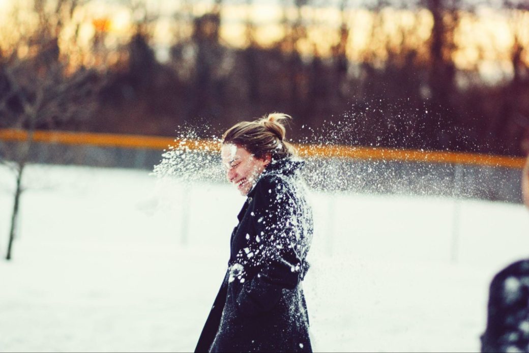 A woman in a coat has just been hit with a snowball: you can see the spray of snow around her
