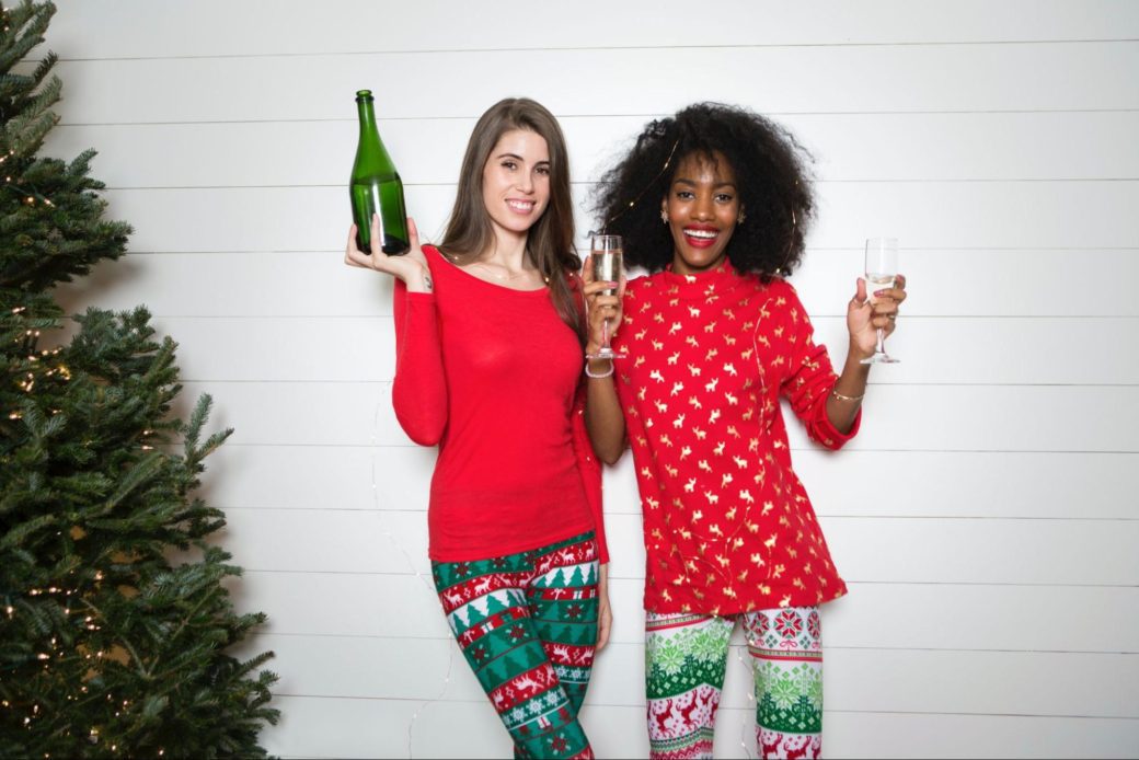 Two women in festive red and green outfits raise glasses of champagne